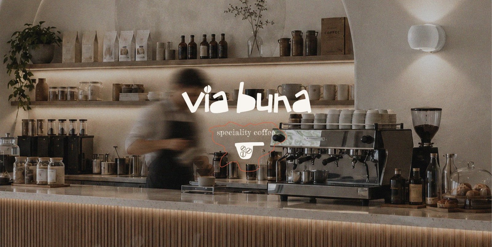Via Buna café counter with espresso machine, shelved retail bags, and a blurred barista in motion
